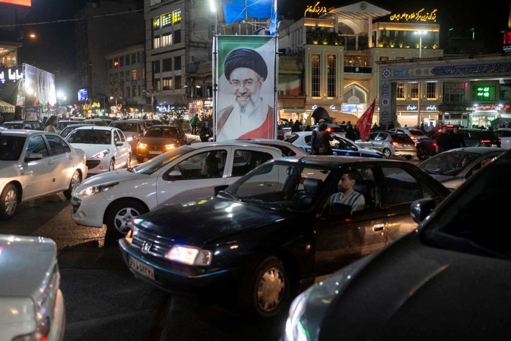 Dòng xe di chuyển qua tấm biển mang chân dung Lãnh tụ Tối cao Iran Mojtaba Khamenei trong cuộc tuần hành ủng hộ chính phủ tại Tehran tối 21/10.